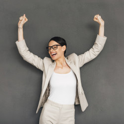 Cheerful young businesswoman in glasses gesturing and keeping her mouth open while standing against grey background